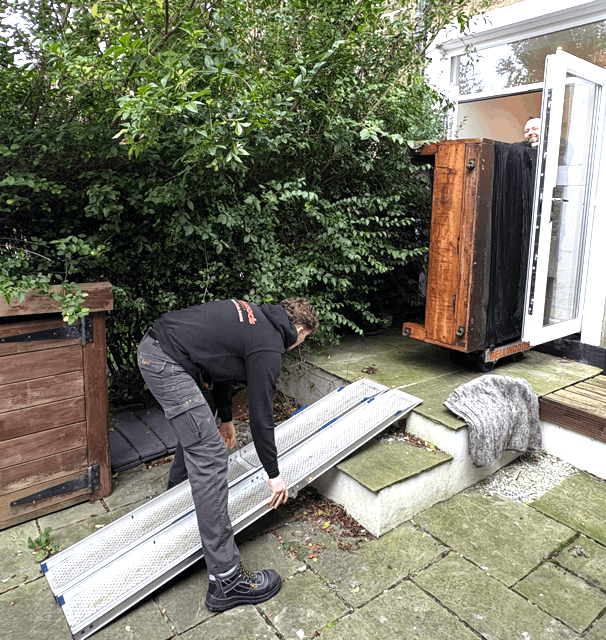 Two movers carefully bringing an upright piano out of a Yorkshire stone cottage